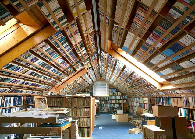 Photo of the top floor of a house with the slated roof and walls all but covered in books in bookcases. 