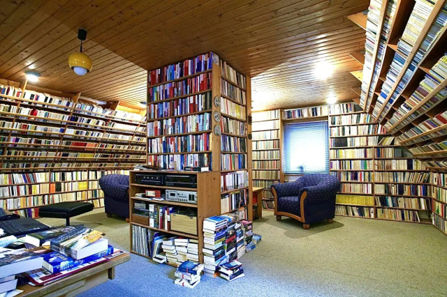 Photo of a room in a house with the walls and center column all but covered in books in bookcases. 