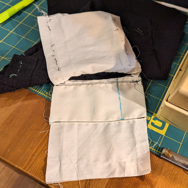 The pocket bag has been opened and a patch pocket laid between the layers. The top and bottom have been hemmed, and the bottom has been stitched to the larger pocket.