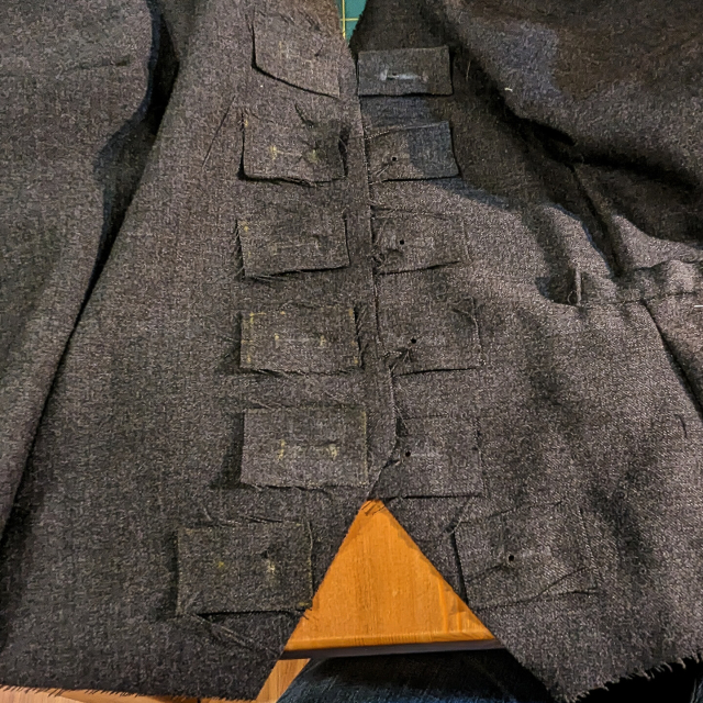 The left front and left front lining pieces of a waistcoat, with self fabric button hole linings stitched down over the button hole markings 