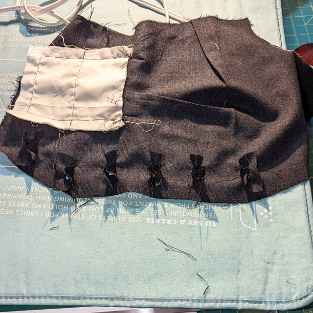 Rectangular button hole linings pushed though the slashed openings along the front piece of a waistcoat.