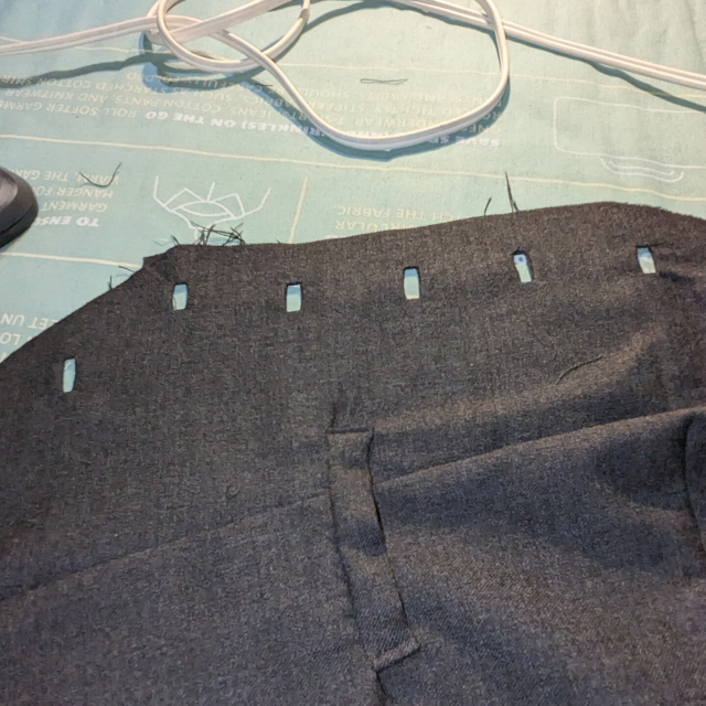 The front of a waistcoat laid out on an ironing board, showing the rectangular openings of new button holes.
