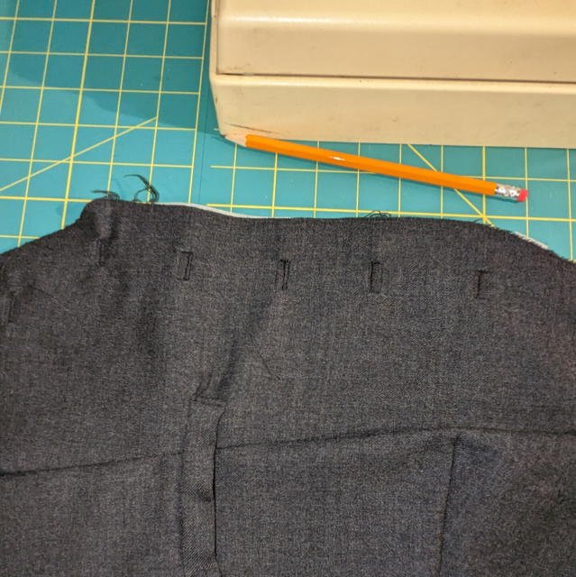 A waistcoat piece with lined button holes sits face up on a green cutting mat