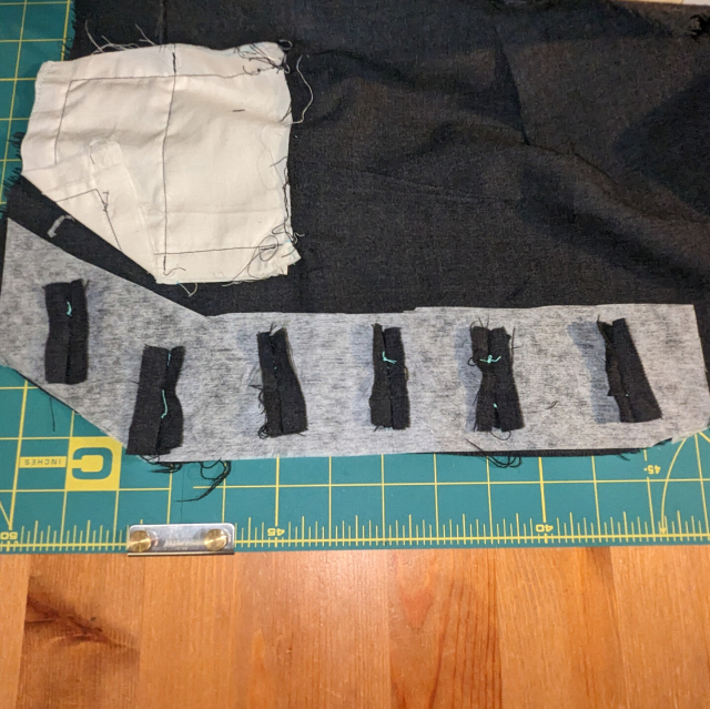 Dark button hole welts hold a piece of interfacing in place on the back of a waistcoat piece