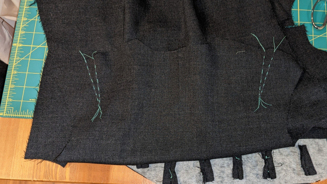 the back piece of a grey waistcoat sitting on a table, with teal stitching marking the shoulder dart lines