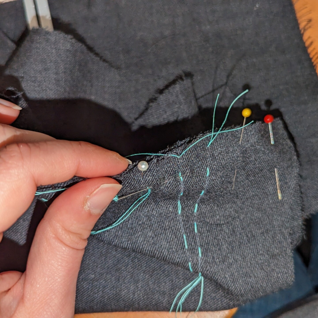 Hand-basting the shoulder seam with bright teal thread, flattening out the ease as I go