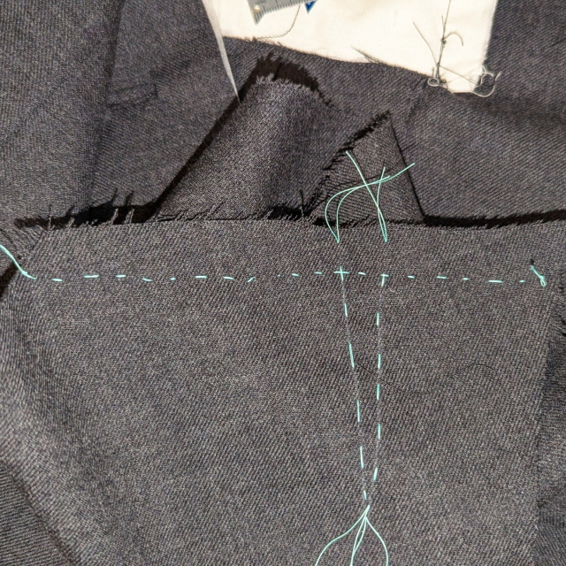 a hand-basted shoulder seam in teal thread on a grey waistcoat
