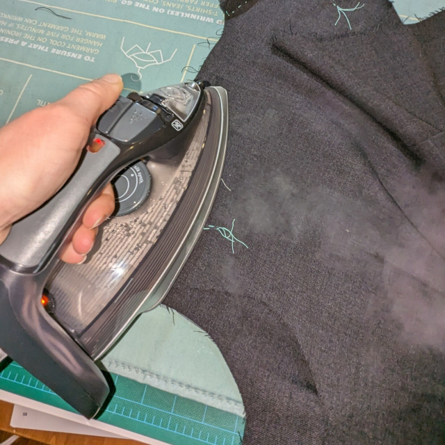 steam drifts out from an iron over the grey waistcoat's shoulder seam.