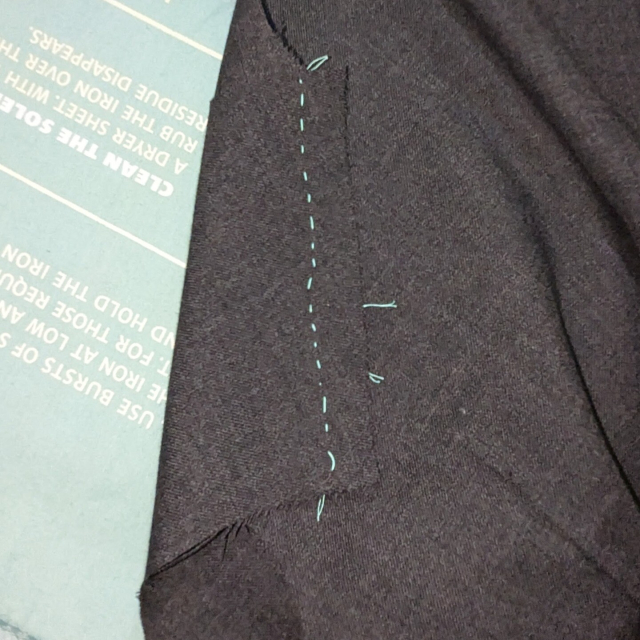 The front of the basted seam, ironed flat. the ends of the thread tracing peak out from underneath, showing the original dart location.