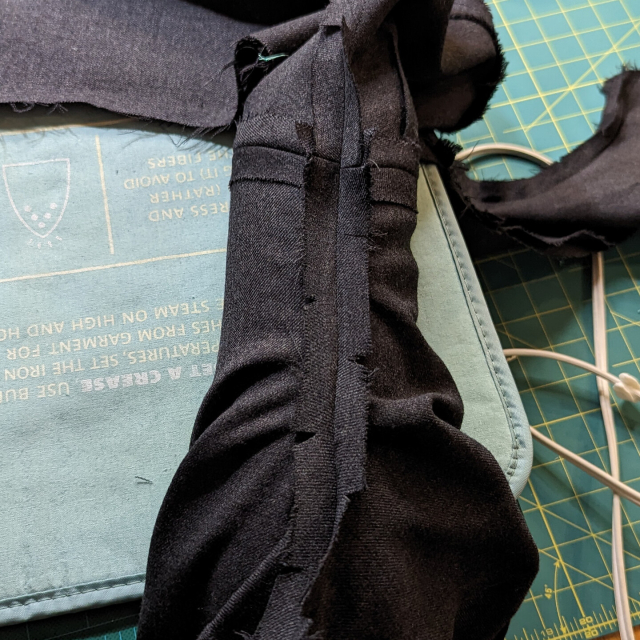 The armscye seam of a grey waistcoat, with a seam roll stuffed inside. The seam allowance has been clipped perpendicular to the stitch line so that it will lie flat.