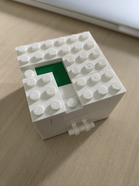 A white cube of Lego bricks. There is a hint of green at the top and a handle on the side