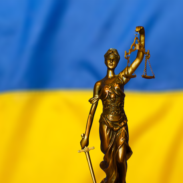 A visual showing the statue of Lady Justice Statue with the Ukrainian flag in the background.