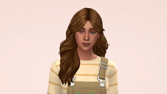 Close-up of a woman with long brown hair, greyish-green eyes, and freckles. She is wearing tan overalls and a cream & yellow striped sweater.