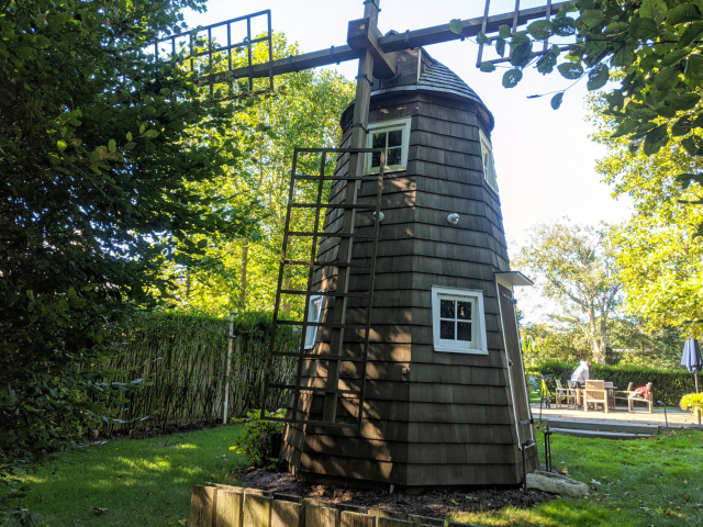 Smock style windmill with sails removed, but blade lattice standing. White frames on the windows. Door to the side