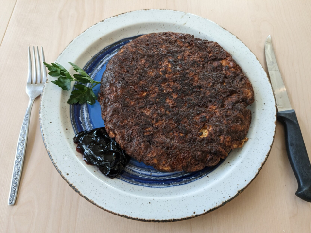 A crusty well-done puck of matza brei with jelly and a sprig of parsley on a plate.