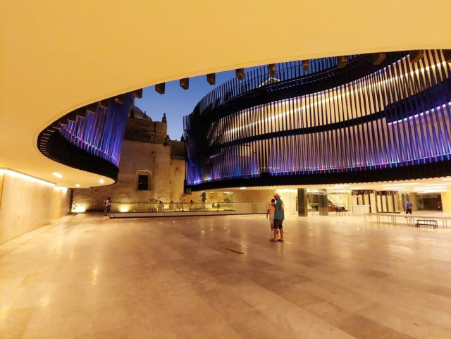 Fotografía del vestíbulo interno del palacio de la música en Mérida, Yucatán.

El espacio está delimitado por dos paredes curvas en una segunda planta y se observa el cielo y edificios coloniales aledaños.

