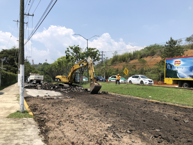 Excavadora abriendo todo el pavimento de la calle. Atrás, un camión de volteo estacionado.