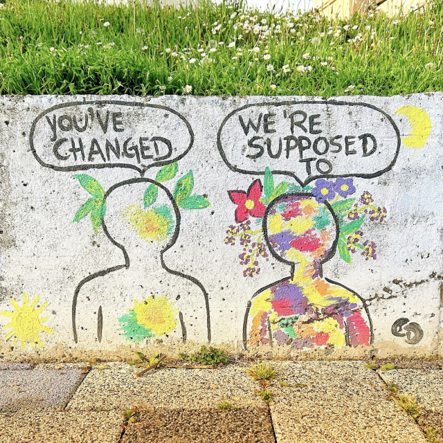 Street art wall painting of two matchstick figures surrounded by flowers. One says, 'You've changed'. The other replies, 'We're supposed to'.