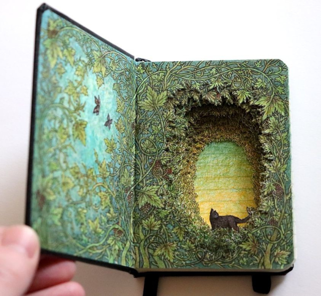 A book transformed by glue and carving to display a three-dimensional cat in a forest, surrounded by vines. 