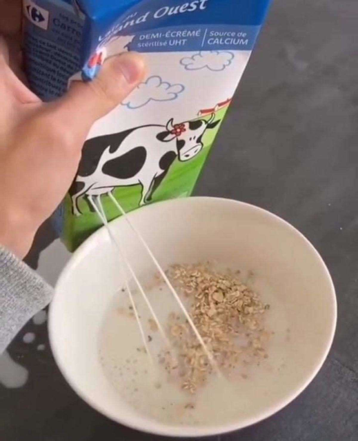 Una persona le pone leche a su avena, el empaque de leche tiene una vaca y la leche brota de las ubres 