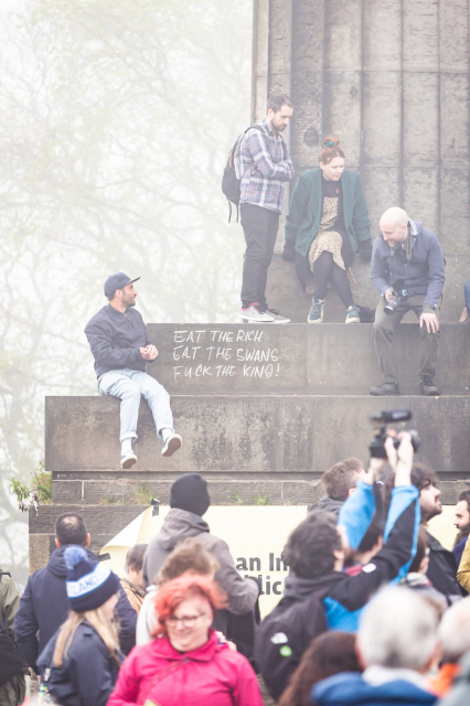 Attendees at the rally for a republic on Calton Hill, Edinburgh. A few people are sat on the monument, where someone has written, in chalk:
"Eat the rich
Eat the swans
Fuck the king!"