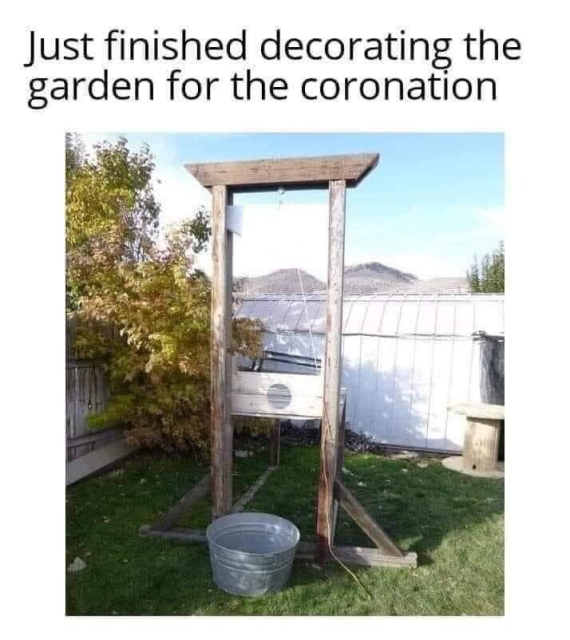 a photo titled “just finished decorating the garden for the coronation”. it pictures a guillotine with a bucket in a nice garden setting. 