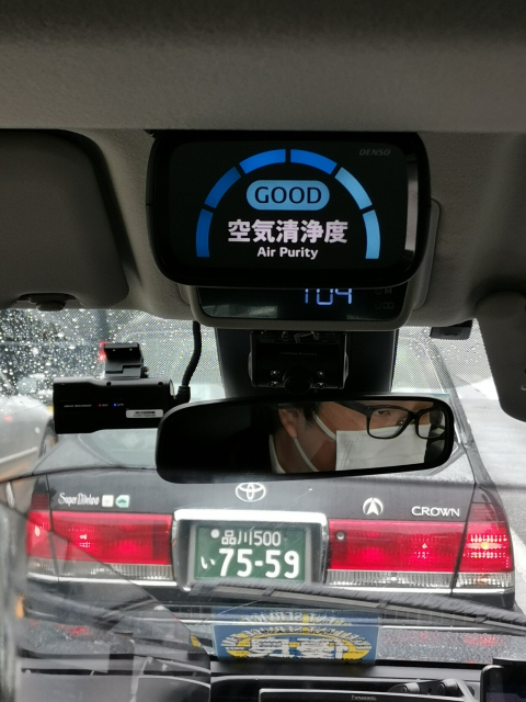 Air quality monitor hanging from the ceiling of a taxi in Japan. It displays Good in blue letters. Another car is visible through the front window. 