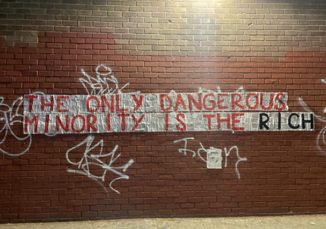 Pasteups on a wall that spell out "The only dangerous minority is the rich"