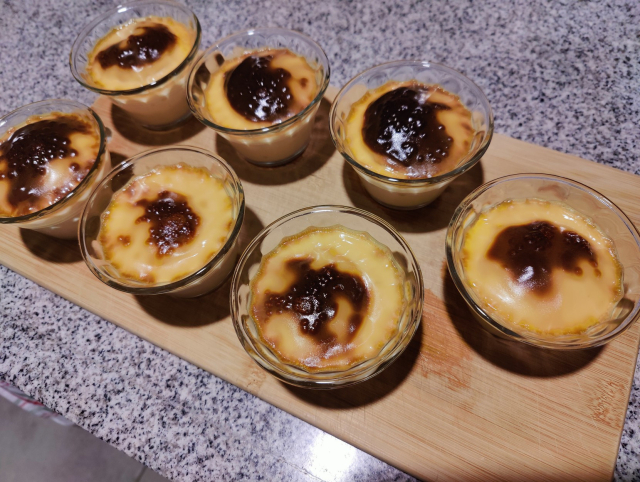 7 postres de jericalla sobre una tabla de madera. Se aprecia la capa superior del postre con una costra quemada.