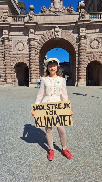 Greta Thunberg, in her graduation dress, posing outside the Swedish Parliament with her School Strike for the Climate sign.