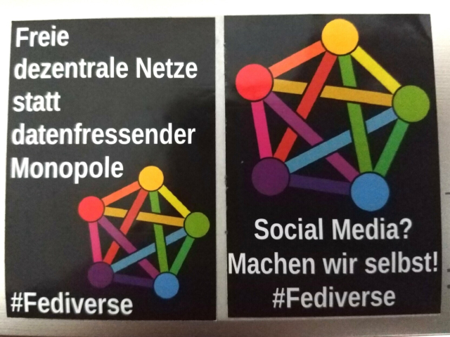 2 schwarze Sticker mit weißer Schrift und dem bunten Fedivers-Logo darauf.

Auf dem linken Sticker steht:
Freie dezentrale Netze statt datenfressender Monopole #Fediverse

Auf dem rechten Sticker steht:
Social Media? Machen wir selbst!