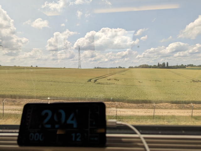 A view from the train window with a mobile phone showing speed 294 km/h