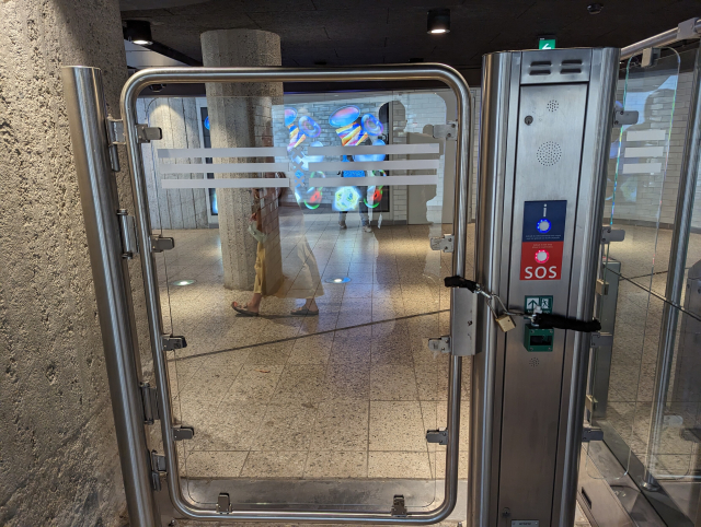 An emergency exit gate in a metro station locked in closed position by a bicycle chain and a padlock.