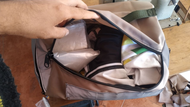 Abriendo la mochila para ver sus contenidos. El cierre principal es más grande que los laterales. Dentro se asoma un jersey, unas bolsas de plástico y un short de lycra