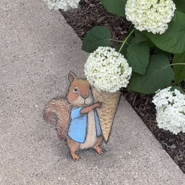 Chalk art of a squirrel hoping an ice cream cone. The scoop is a real hydrangea.