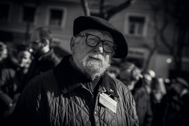 Retrato en plano medio-primer plano en blanco y negro de uno de los manifestantes, un señor mayor barbudo ataviado con gafas y boina. Columna este de la Manifestación por la Sanidad en Madrid que sale desde el Hospital de La Princesa. 