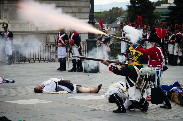 Recreaciones del Dos de Mayo en la Plaza de Oriente en Madrid. 

Imagen en la que se ve a un restos de tropas napoleónicas descargando sus rifles. Se ve la ristra de pólvora y la chispa ardiendo de los rifles. Se ve a gente en el suelo simulando los caidos en combate