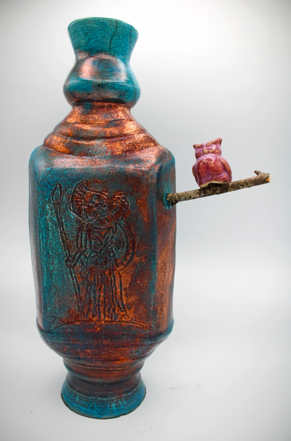 A blue and copper raku vase/vessel with Athena etched on the front with a small stick on the side with a clay owl on it.