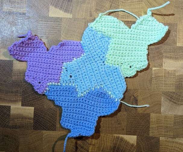 Four crocheted monotiles in purple, light blue, dark blue, and green, on a wooden countertop.