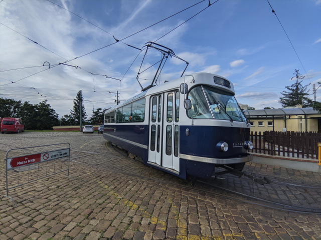 T3 Coupé from outside standing in Střešovice depot.
It is a Tatra tram originally designed in 1960, that was redesigned by Anna Marešová in 2017. It has blue and silver metallic paint. It has roof windows inspired by old Škoda RTO buses. The back of the vagon has no windows in summer.
