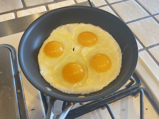 A fry pan with four sunny-side-up eggs in it
