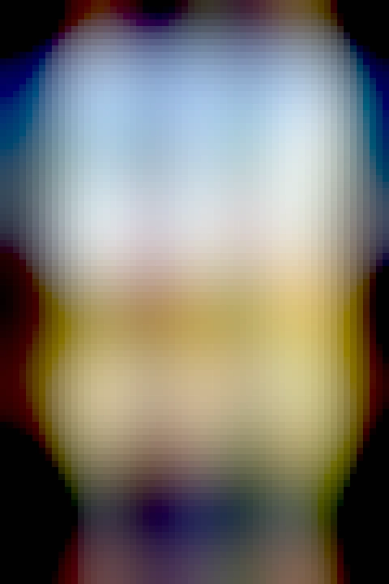 A colour photograph of the view from a castle. Blue sky with white clouds, and yeelow/green fields with drystone walls running through them are framed by the castle's stone walls. 