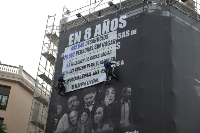 Dos activistas descuelgan varias pancartas sobre la lona de desokupa con los lemas:
"En 8 años...
482.549 desahucios
28.552 personas sin hogar
3,8 millones de casas vacías
80% del suelo para alquiler
El problema no es la okupación"