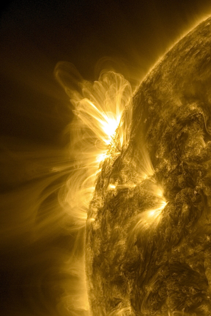 Der Bereich links oben am Rand der Sonne in gelber Farbe und stark ins Bild gezoomt. Da schießt Sonnenmaterie von einer Stelle spektakulär ins All und bildet unzählige feine Bögen entlang der Magnetfelder. Sie überlagern sich dabei, reichen weit ins All und zurück zur Oberfläche.