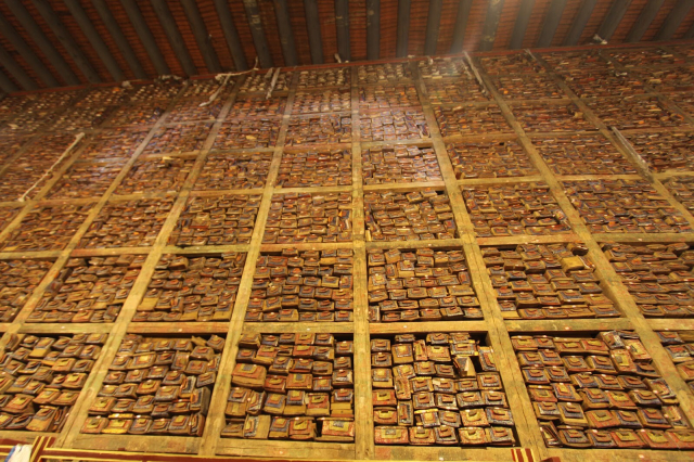Looking up at a very tall wall of books/scrolls inside of small boxes which are grouped inside of cubes. Everything is mostly brown with splashes of bright colors.