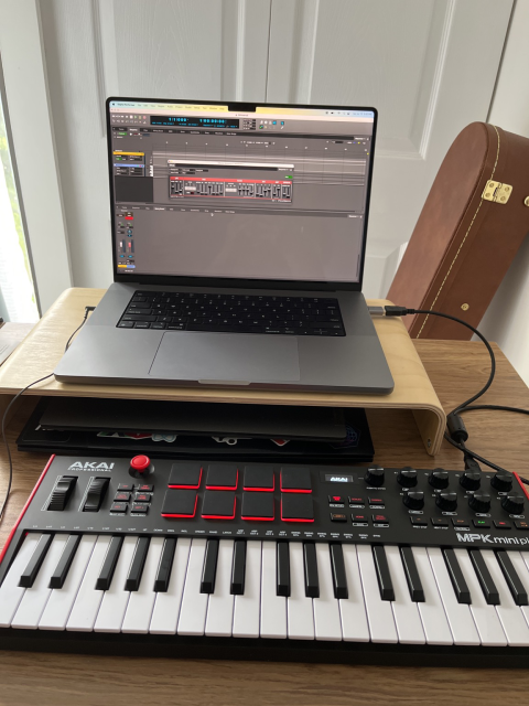 An Akai MIDI keyboard connected to a MacBook laptop running a music recording software 