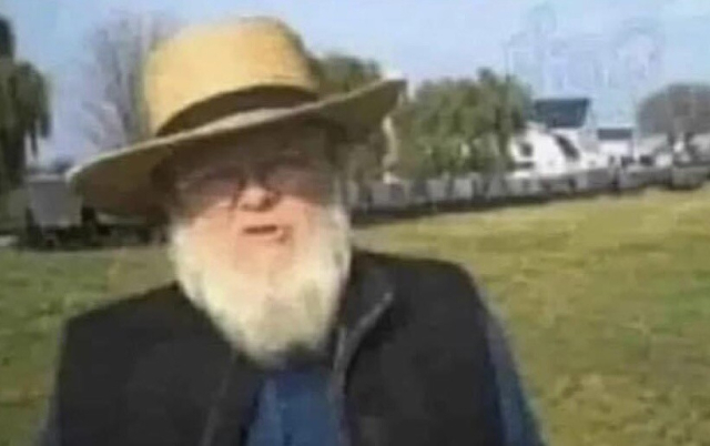 A photo of an elderly person with a thick grey beard, wearing a straw hat. 