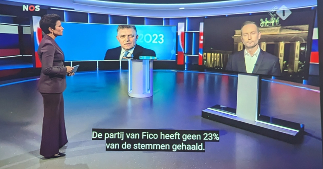 A screenshot from NOS Journaal showing studio anchor, image of Robert Fico and a TV screen with remote correspondent.