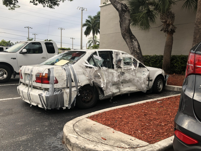 A white sedan in a parking spot. Or at least I think it was once a white sedan as it's now held together by an unbelievable amount of tape.