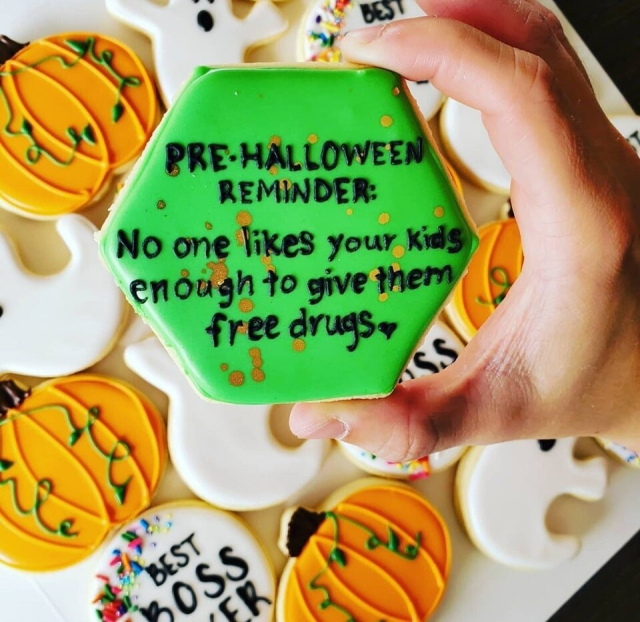 An hexagon-shaped green iced cookie with black writing on it that reads, "Pre-Halloween Reminder: No one likes your kids enough to give them free drugs"